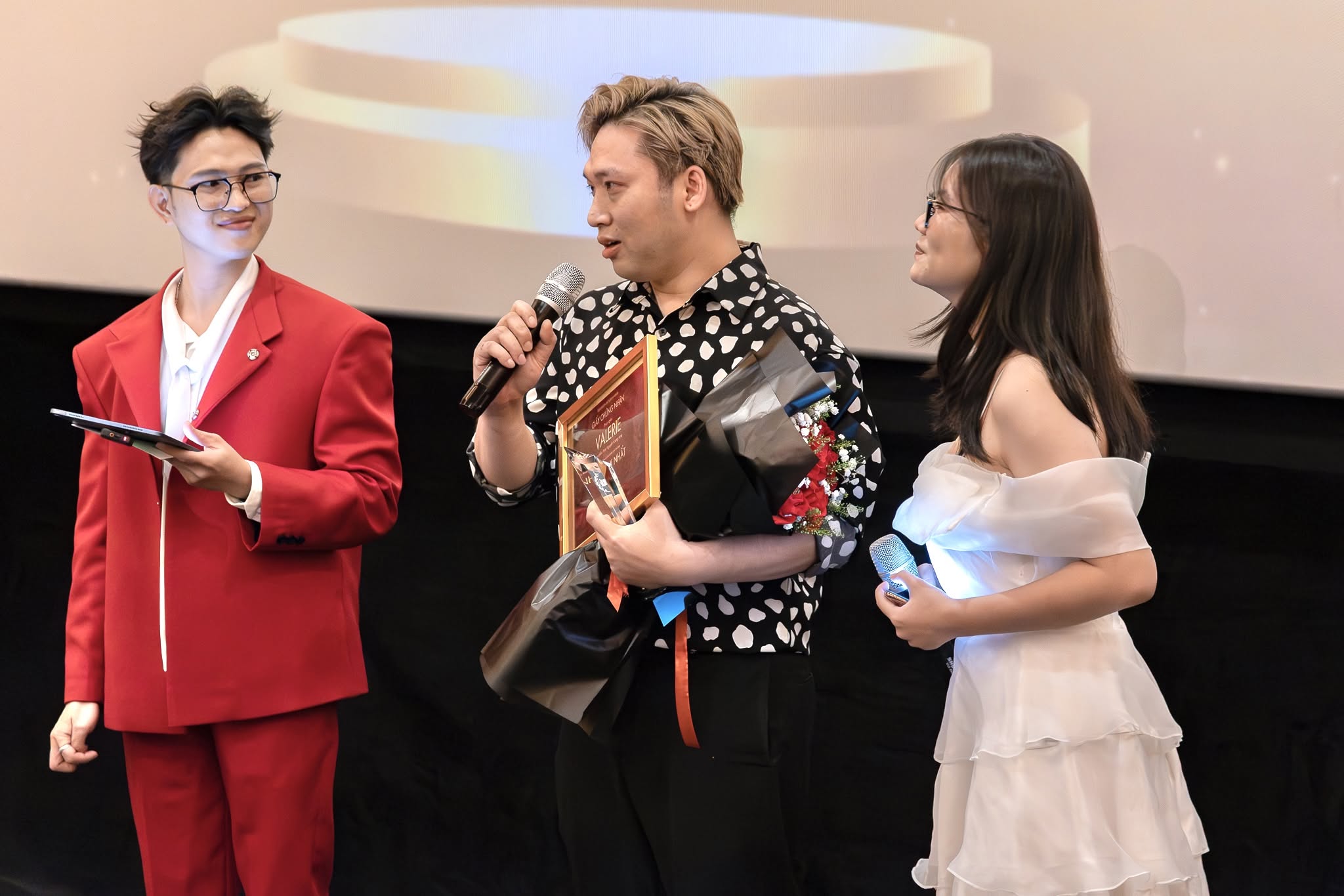Khoảnh khắc người nhận giải phát biểu cùng hai MC, cầm kỷ niệm chương và hoa tại Gala Phim Ngắn 14 Ngày 2025
